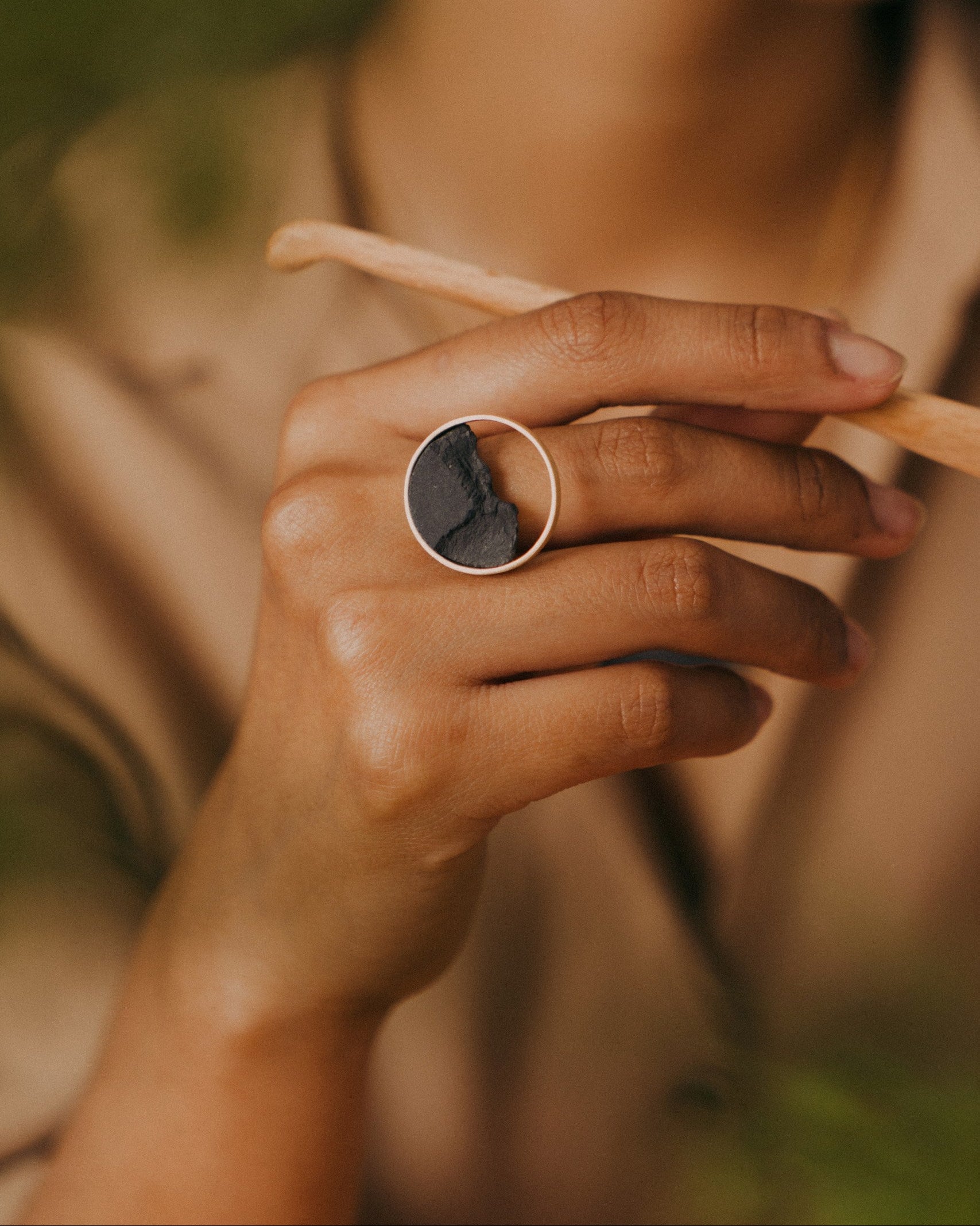 Close-up of a hand wearing a ring with a natural stone, held against a blurred background.